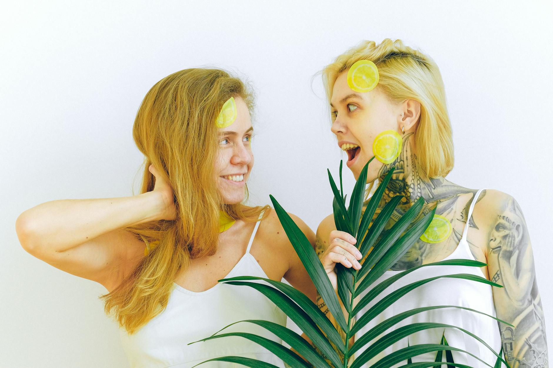 Two women smiling and holding fresh lemons together, expressing comfort and joy indoors