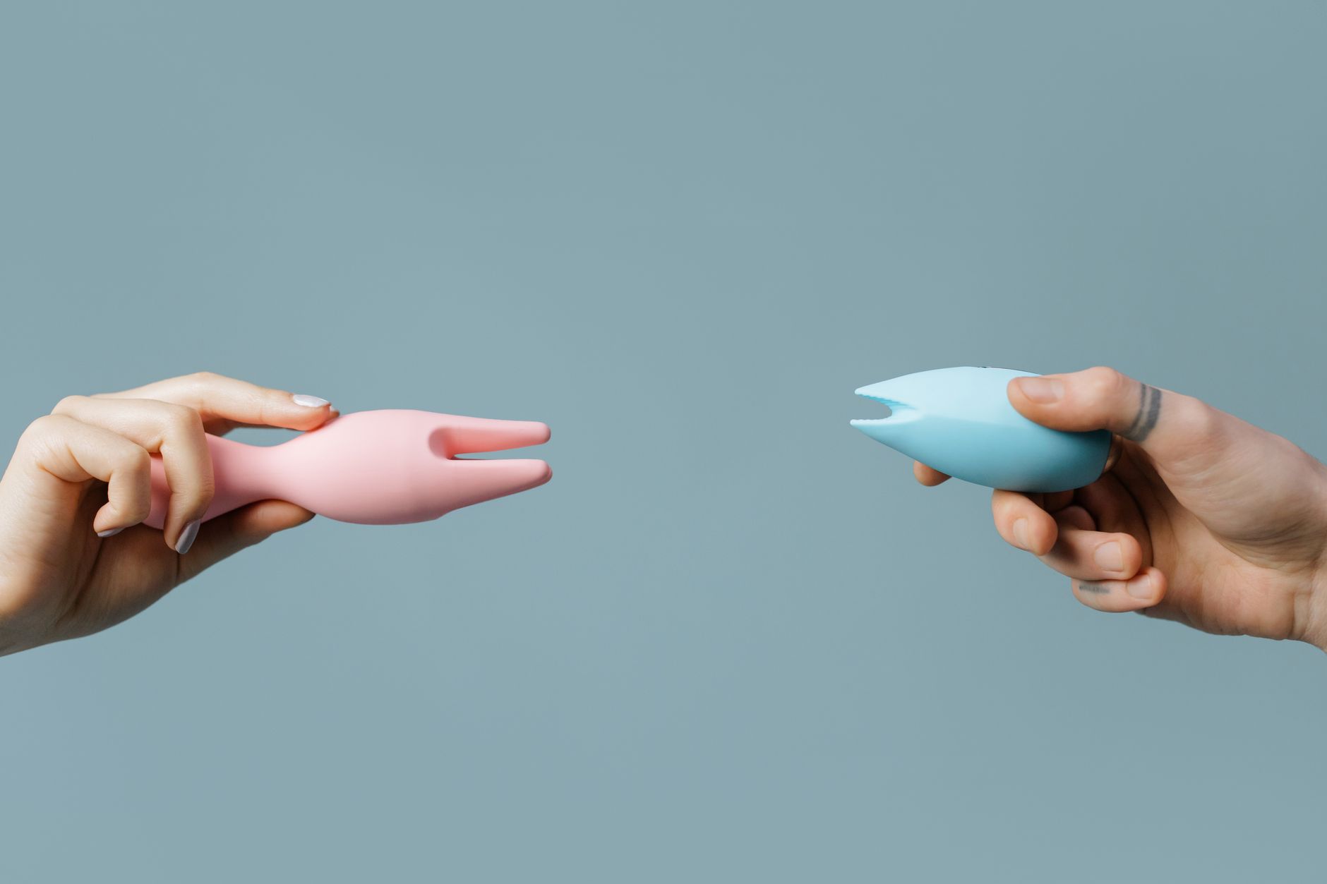 Two hands holding pink and blue vibrators together
