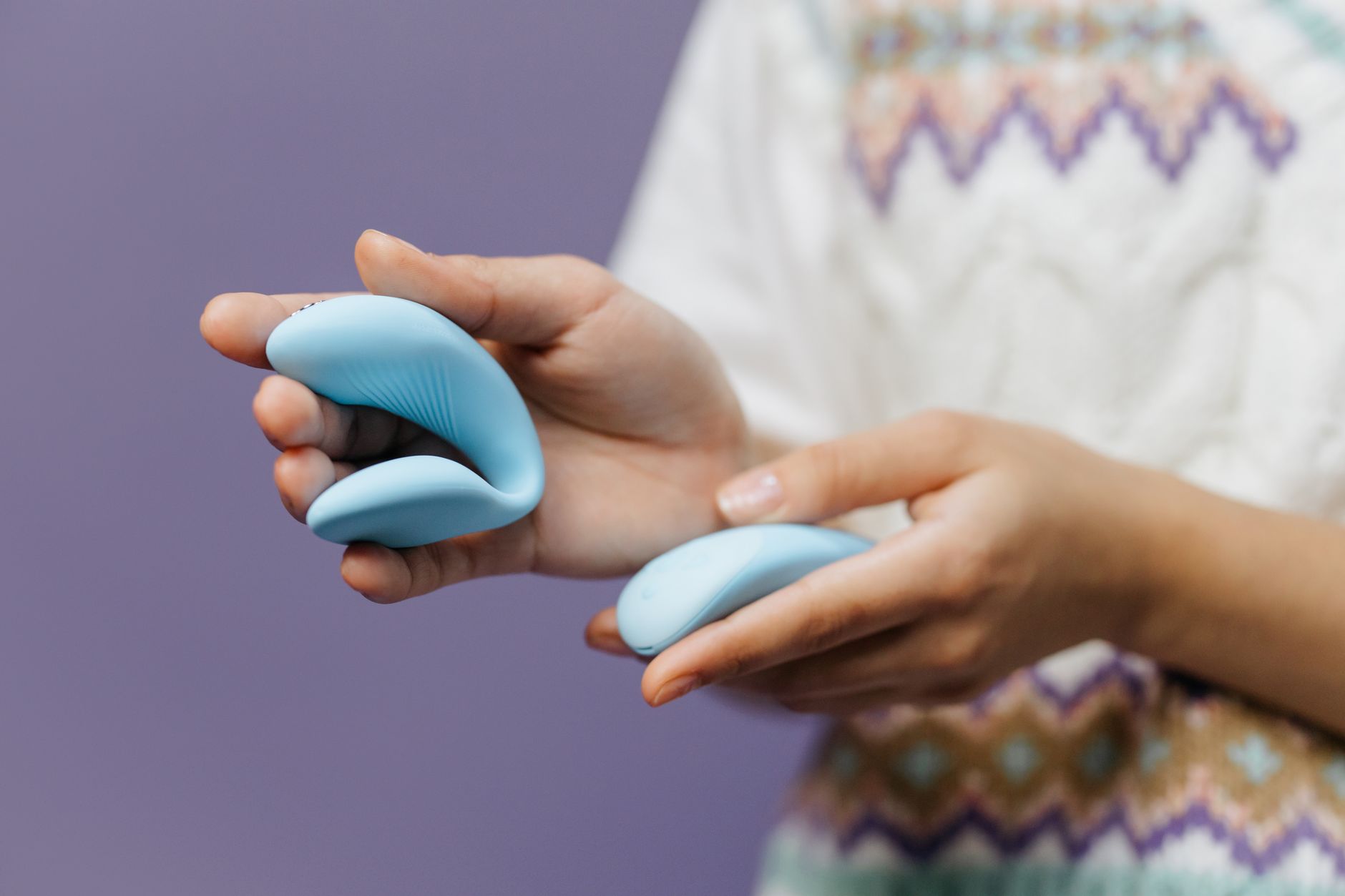 Enger Ausschnitt von Händen, die einen eleganten blauen Vibrator halten, vor violettem Hintergrund