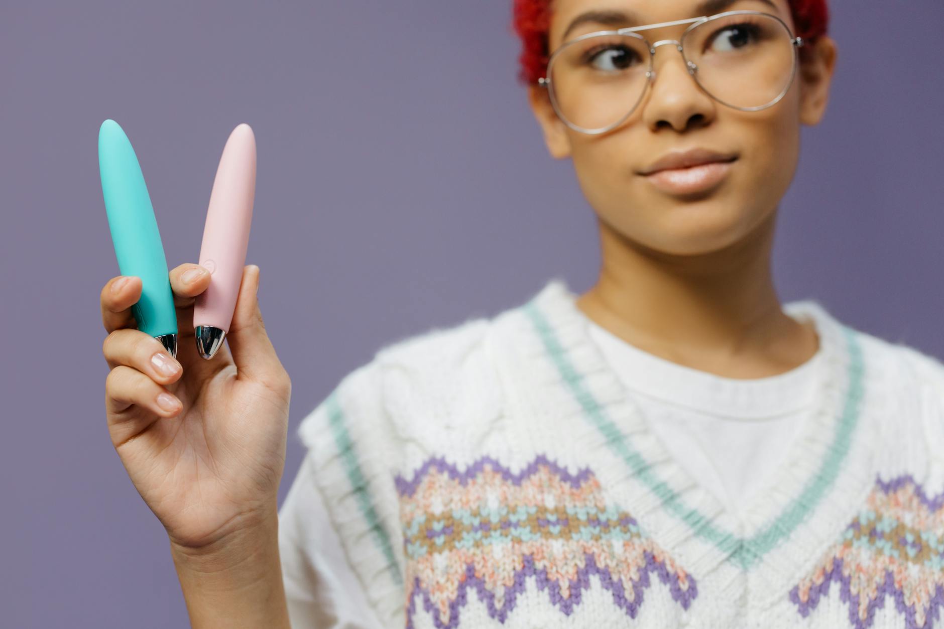 Close-up of hands holding a sleek blue vibrator against a purple background