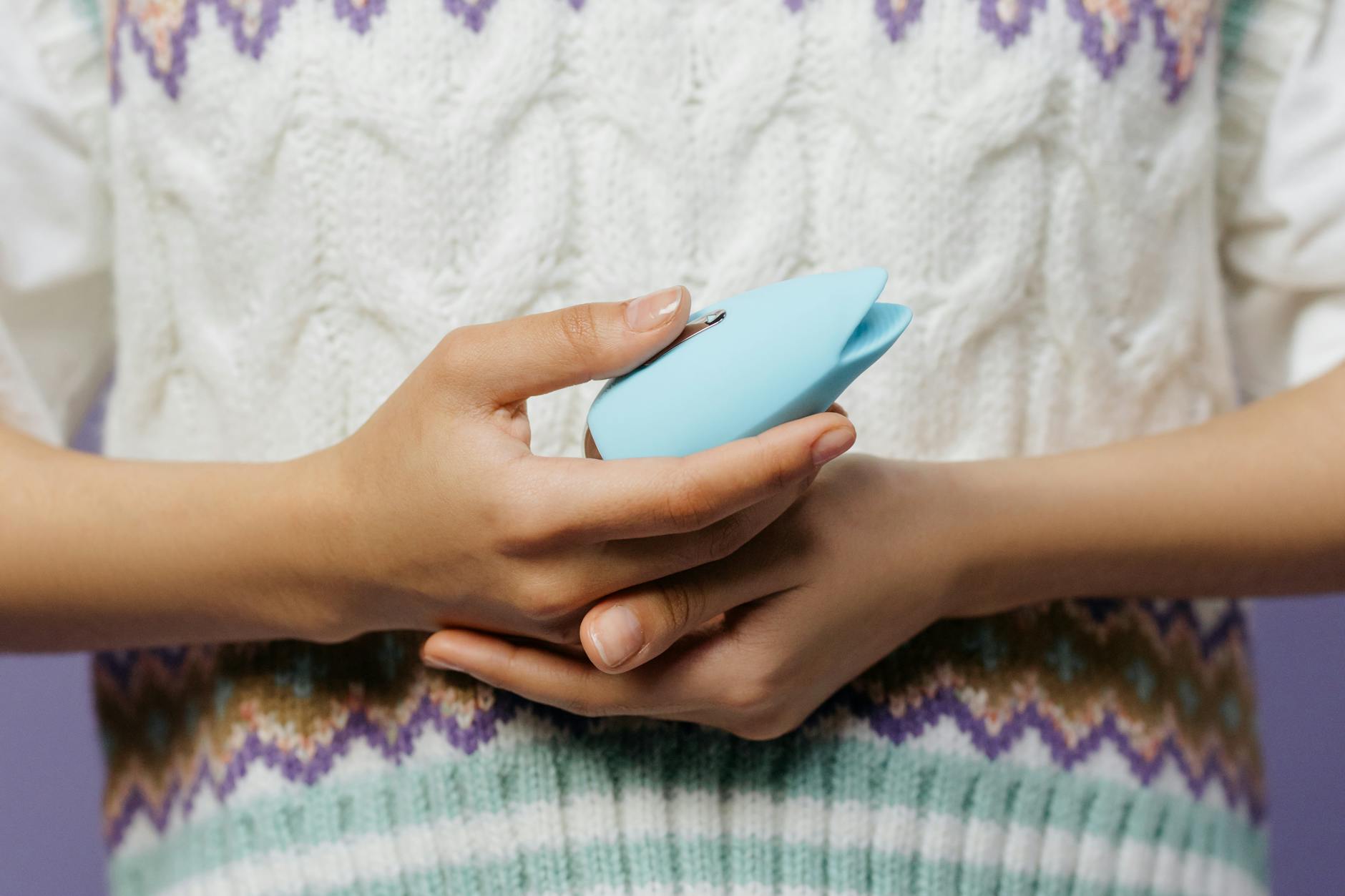 Hands holding a blue Lemon vibrator against a cozy knitted sweater